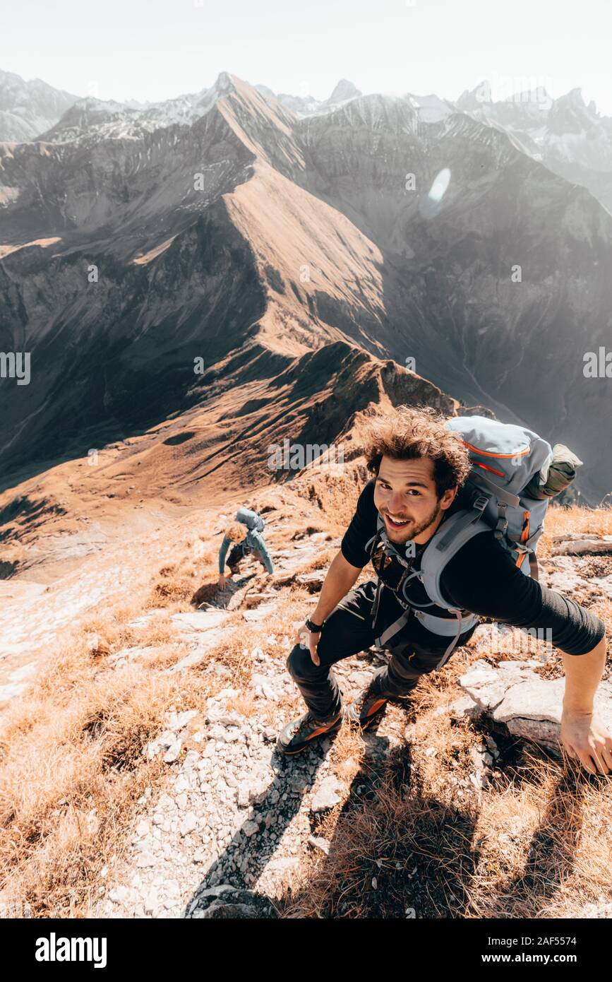 Young hiker climbing a steep mountain path in front of mountains Stock Photo