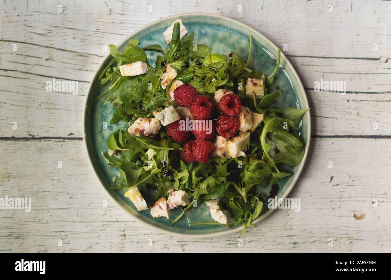 Wild vegetable salad with raspberries and goat cheese, olive oil and modena vinegar, on a white wooden background Stock Photo
