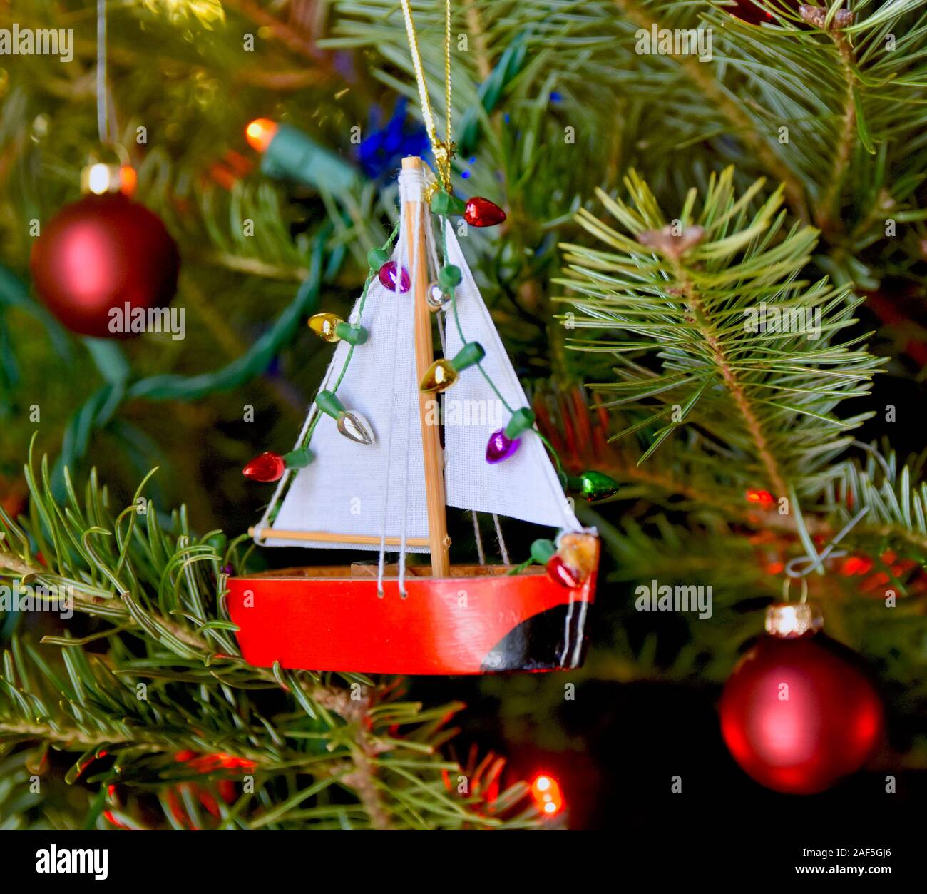 Little red sailboat ornament hanging on a Christmas tree. Closeup. Stock Photo
