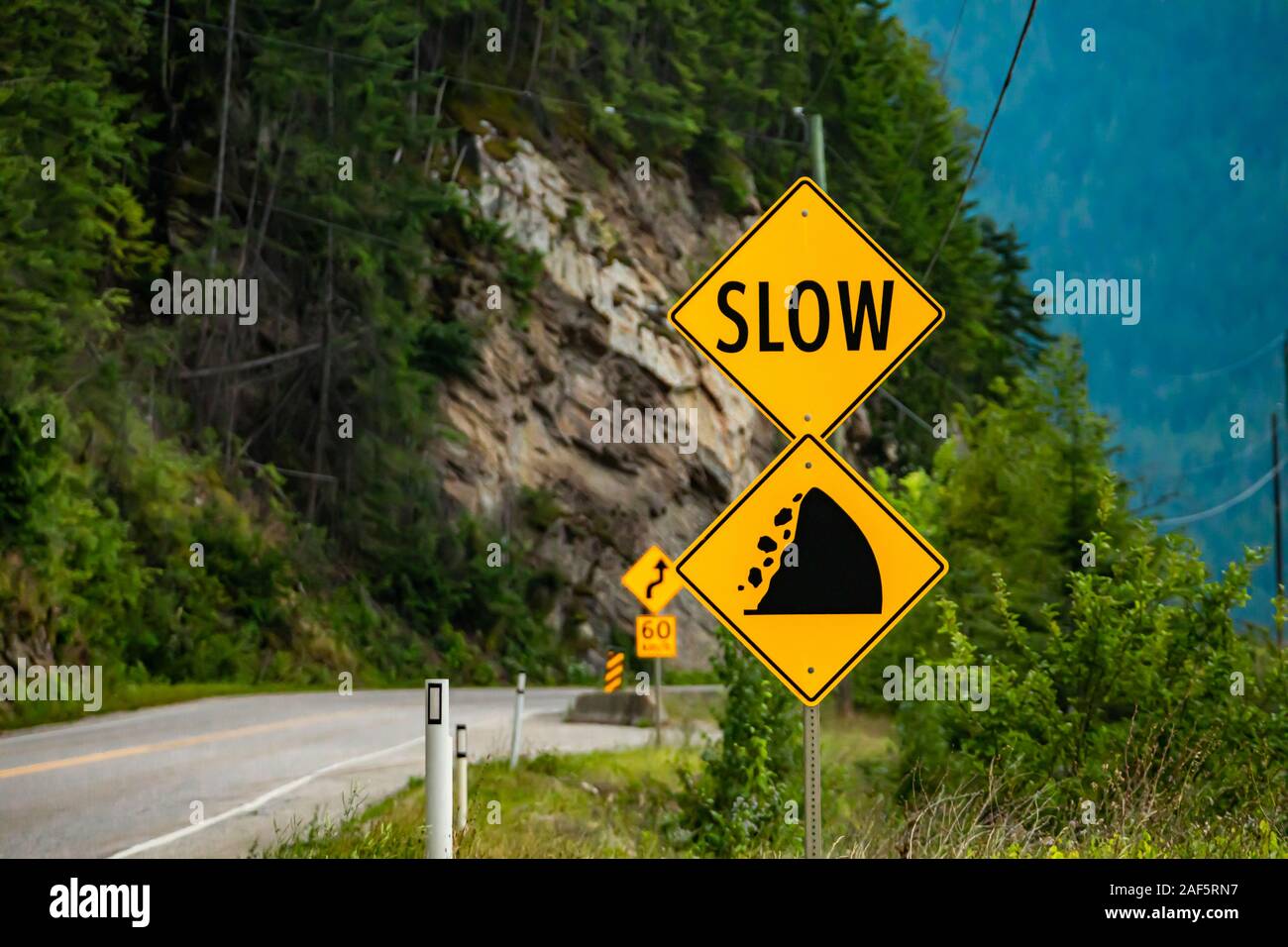slow, Watch for fallen rock and be prepared to avoid a collision, Warning yellow roads signs in selective focus view with rocky slope background Stock Photo