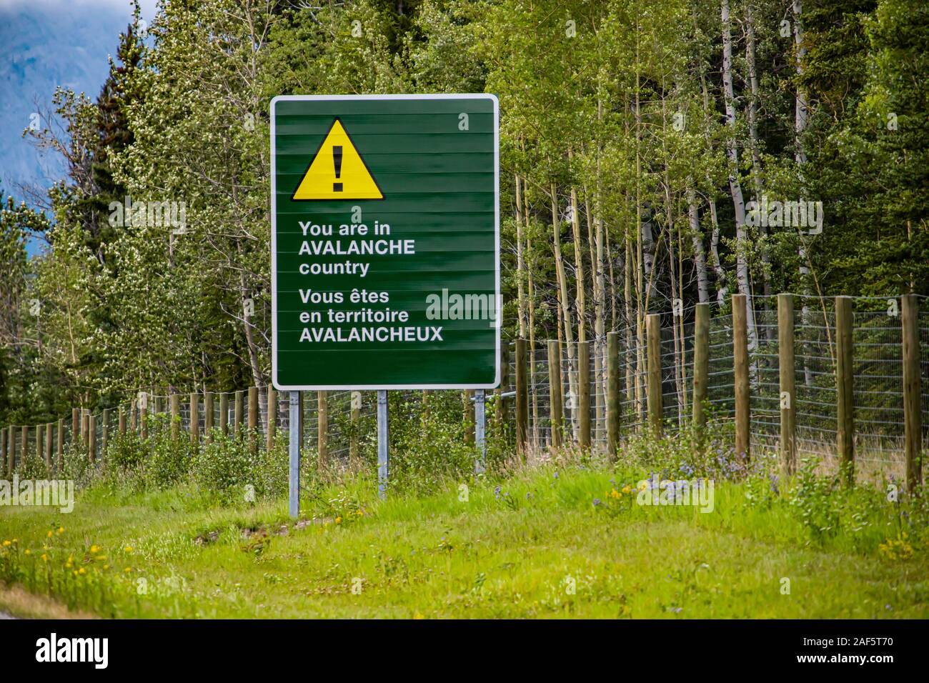 two languages French and English Information road Bilingual green sign on roadside, you are in avalanche country with Yellow warning triangle symbol Stock Photo