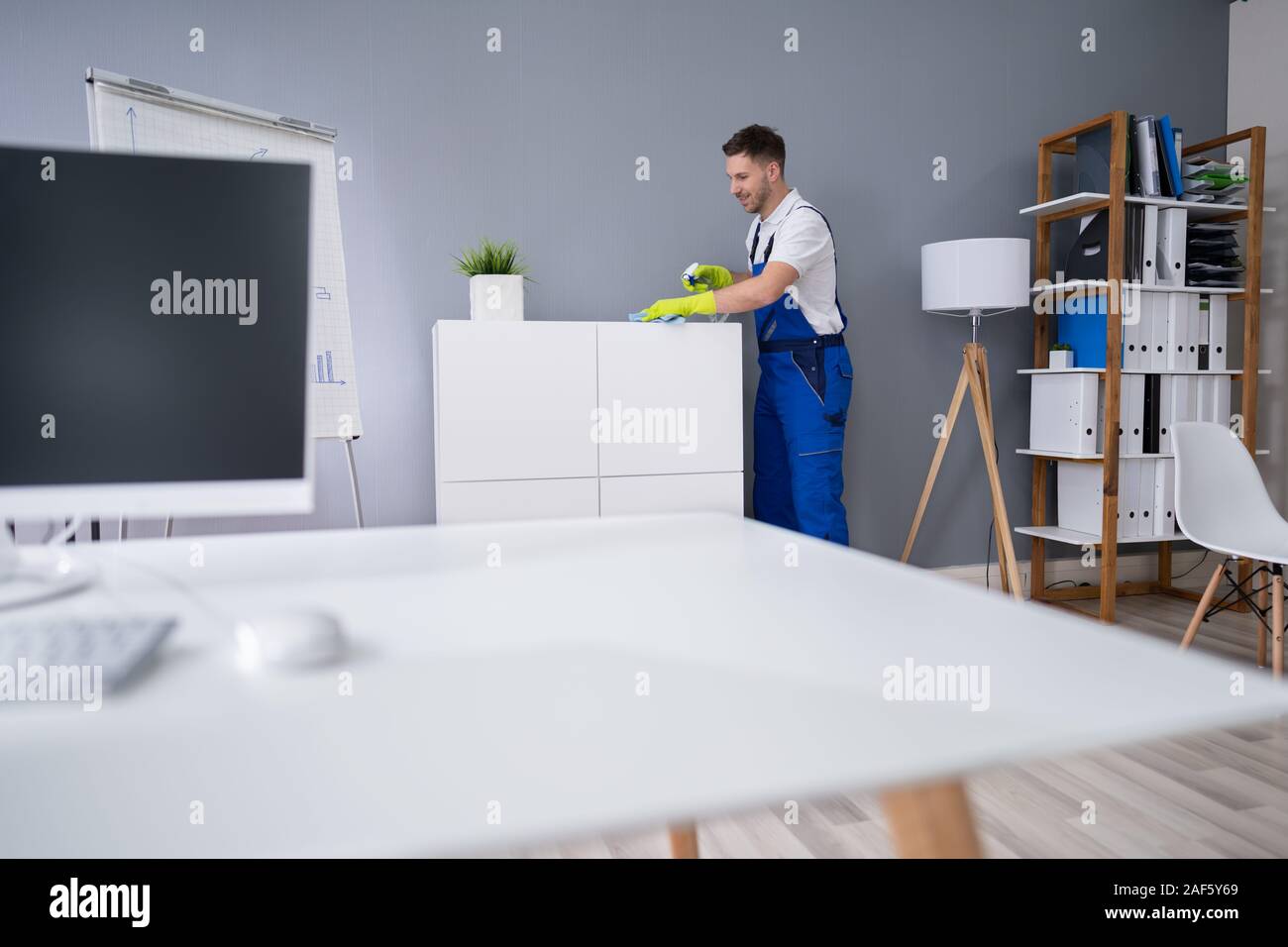 Mid Adult Male Worker Cleaning Shelf With Spray And Sponge At Office Stock Photo