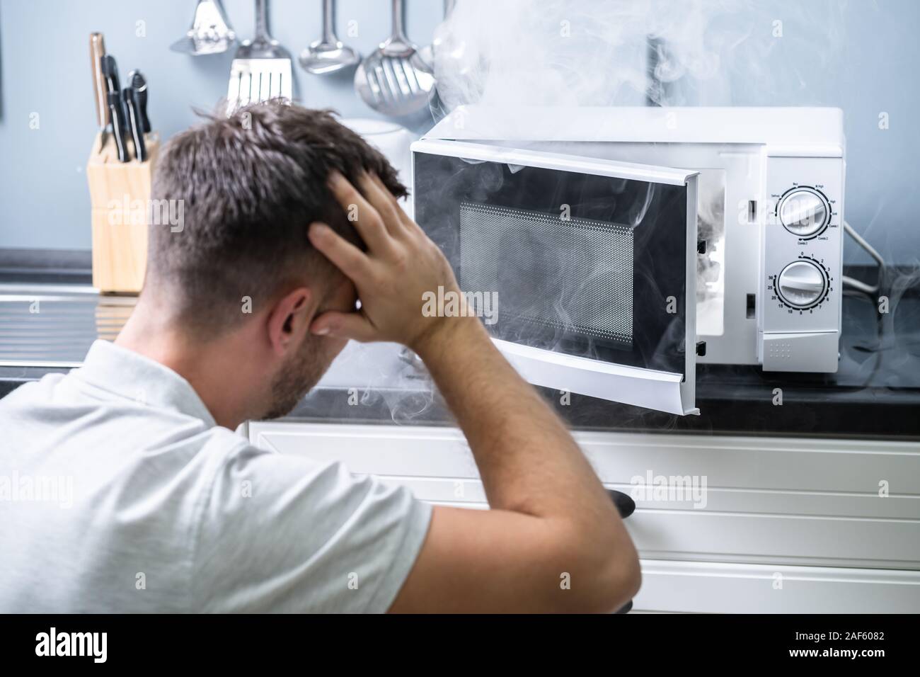 Young Man Spraying Fire Extinguisher On Microwave Oven In The Kitchen Stock Photo