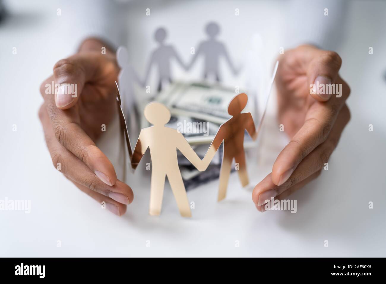 Person's Hand Protecting Stacked Banknotes Surrounded By Human Figures Stock Photo