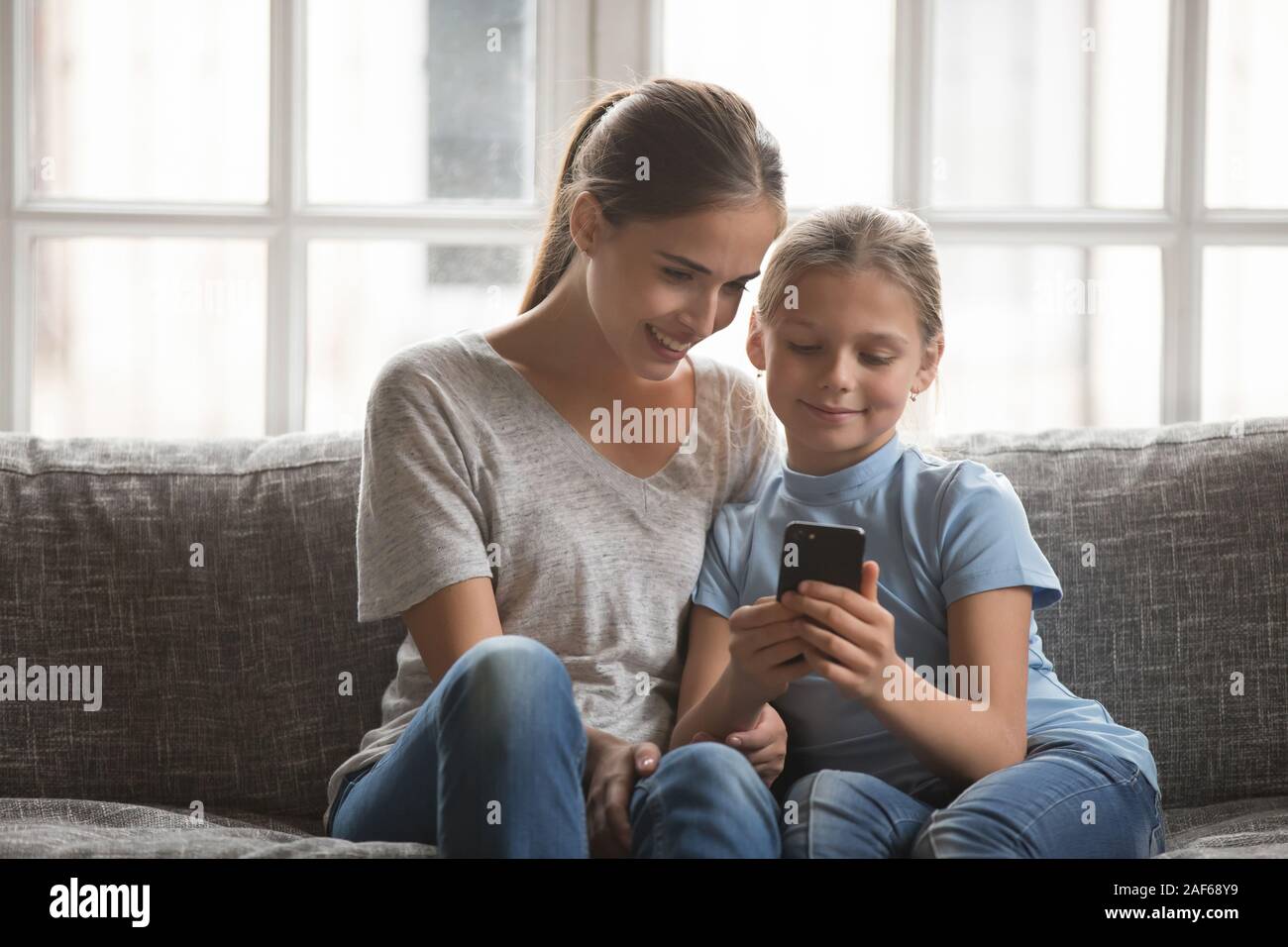 Smiling young mom and daughter using cellphone at home Stock Photo - Alamy