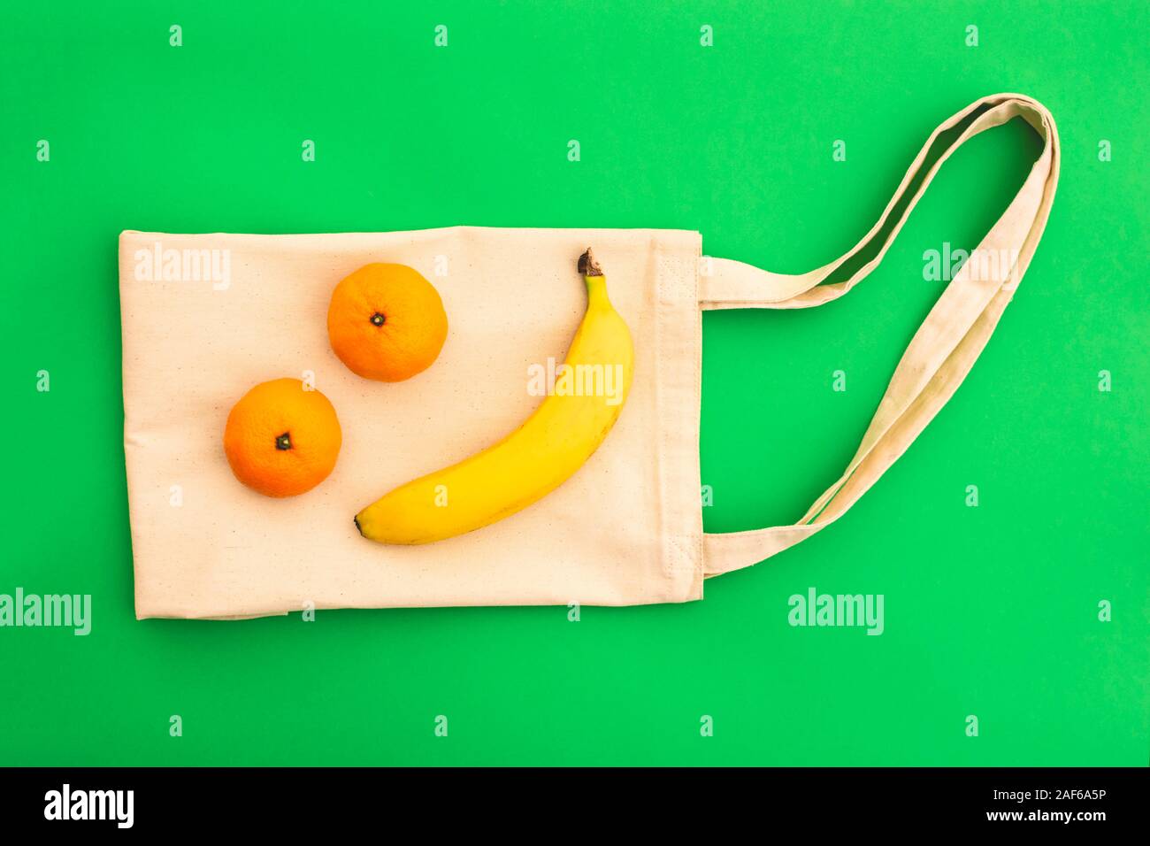 Canvas cotton white bag and banana with tangerines on the bright green background. Eco Friendly reusable bag for shopping. Eco and zero waste concept. Stock Photo