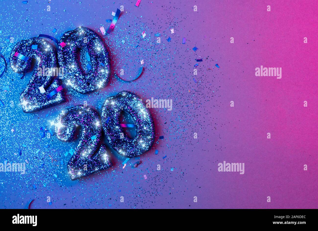 New years 2020 3d numbers flat lay with confetti and christmas bulbs lit by vivid blue and pink lights - new years holiday concept image with copy spa Stock Photo