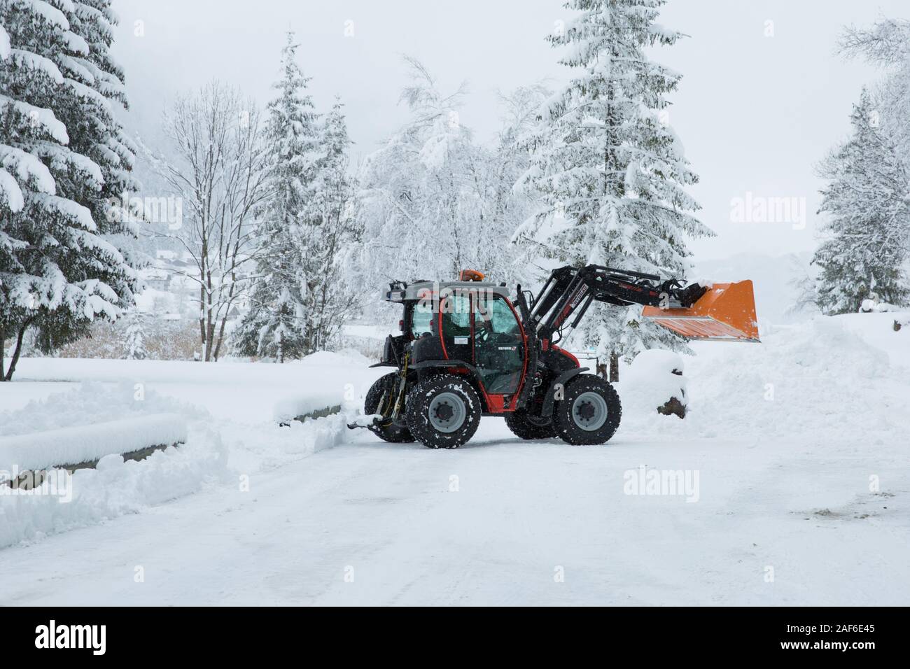 Tractor removing snow from the winter road.Large red tractor with snow plow grader clears snow covered road in mountains, Weissensee, Alps, Austria Stock Photo