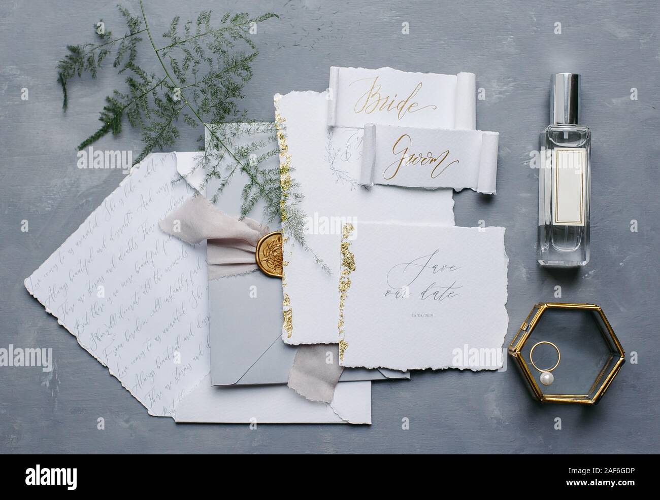 Wedding details flat lay. Wedding invitation and scroll paper. Bottle with fragrance. Simple bouquet. Ring box. Stock Photo