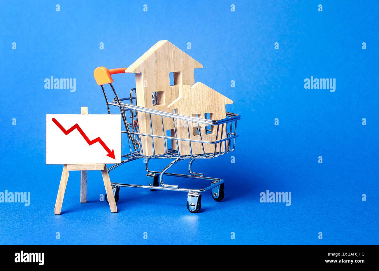 Wooden houses in a shopping cart and an easel with a red down arrow. Fall of real estate market. Cheap rent. Reduced demand, recession. Low sales. Val Stock Photo