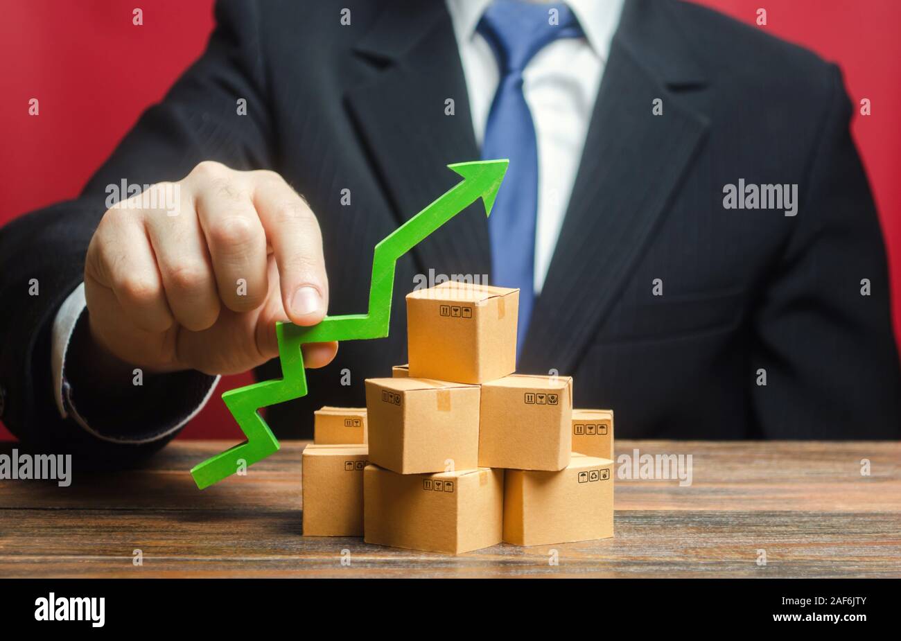 Businessman holding a green arrow up over boxes. Boost sales rate. Increasing production of goods, expanding export opportunities, finding markets. Ta Stock Photo