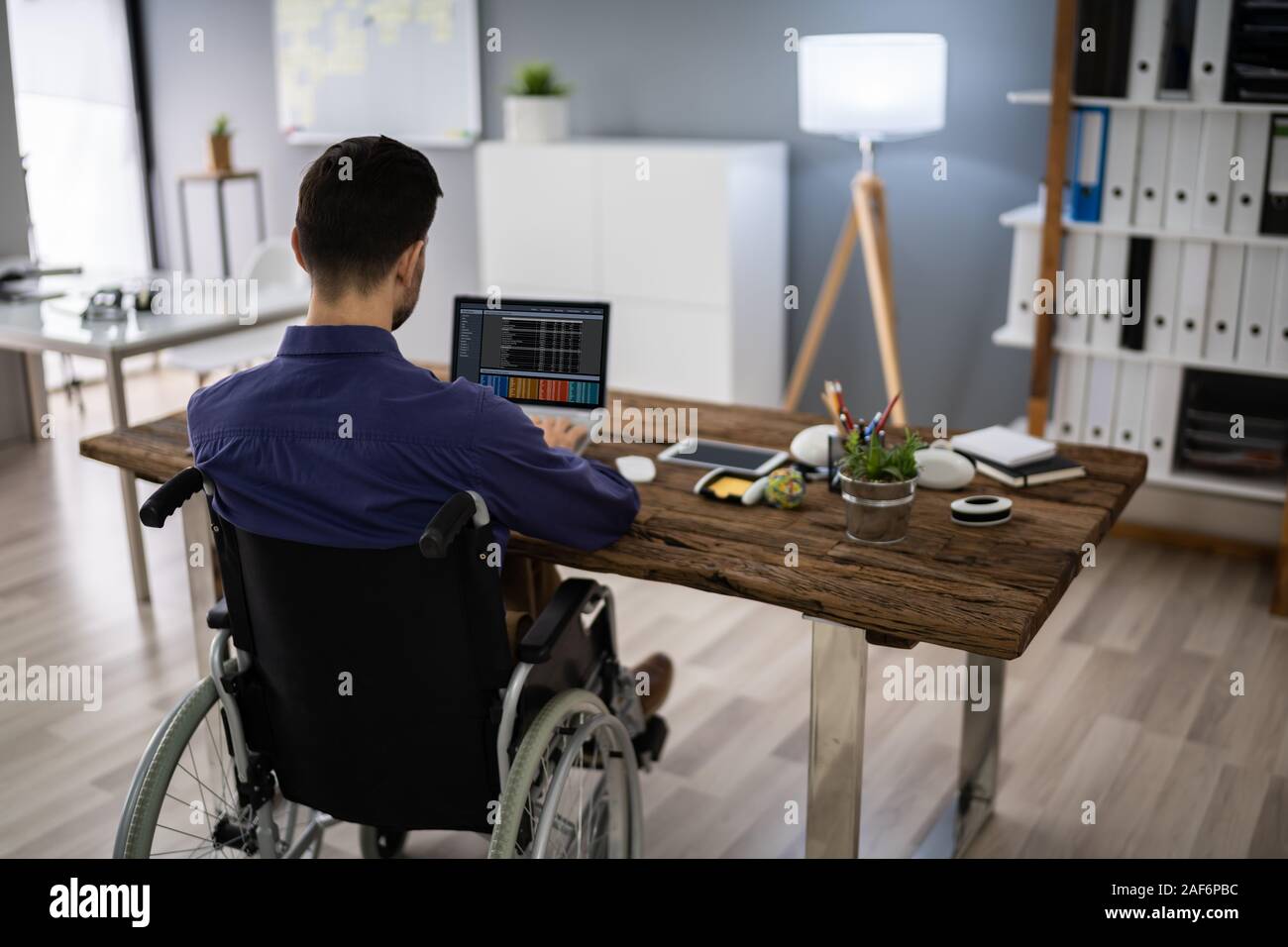 Businessman On Wheelchair While Working On Computer Stock Photo