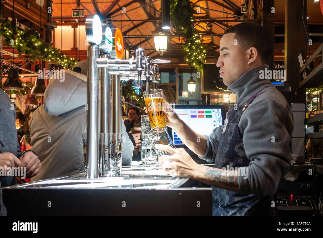 A barman pours a beer for a customer in Mercado San Miguel, an indoor market in Madrid, Spain, seen here on the evening close to Christmas. Stock Photo
