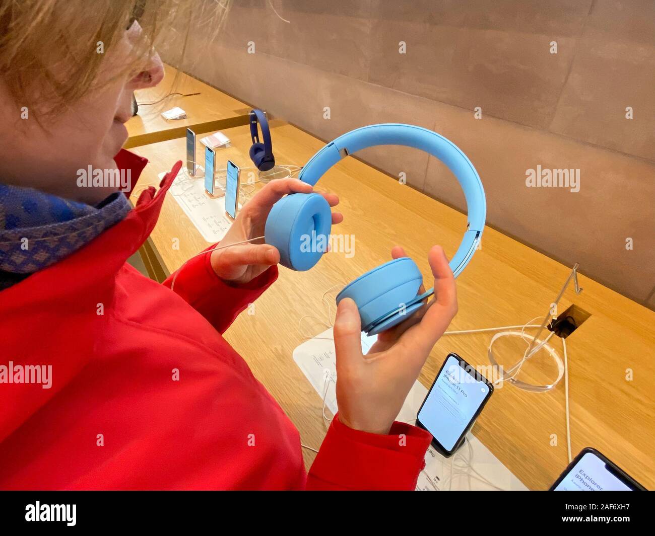 Paris, France - Nov 02, 2019: Woman in red coat inside Apple Computers Store testing the new latest Beats by Dr Dre Solo Pro Active Noise Cancelling headphones Stock Photo
