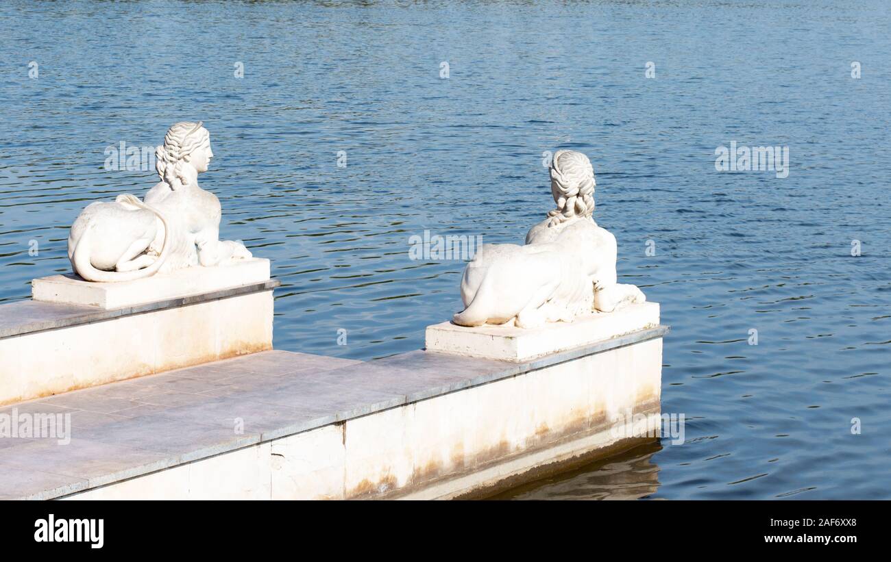 Stone pier with plaster sculptures pond lake. Sphinx sculpture with the