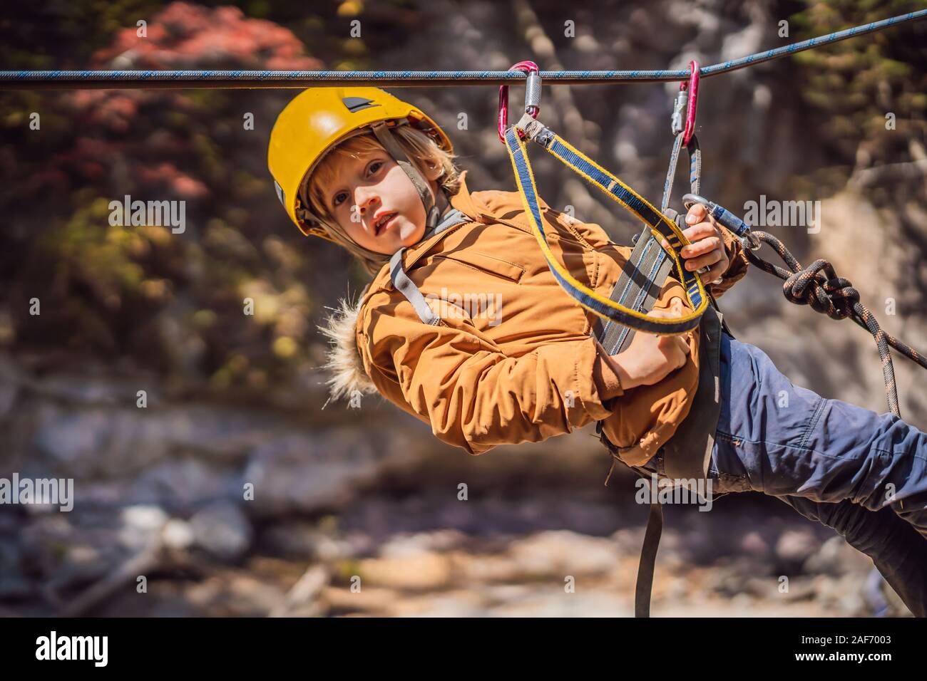 Brave little boy rappelling high among the trees in an Adventure Park for children. Extreme kid. The boy goes down the rope on a carbine Stock Photo