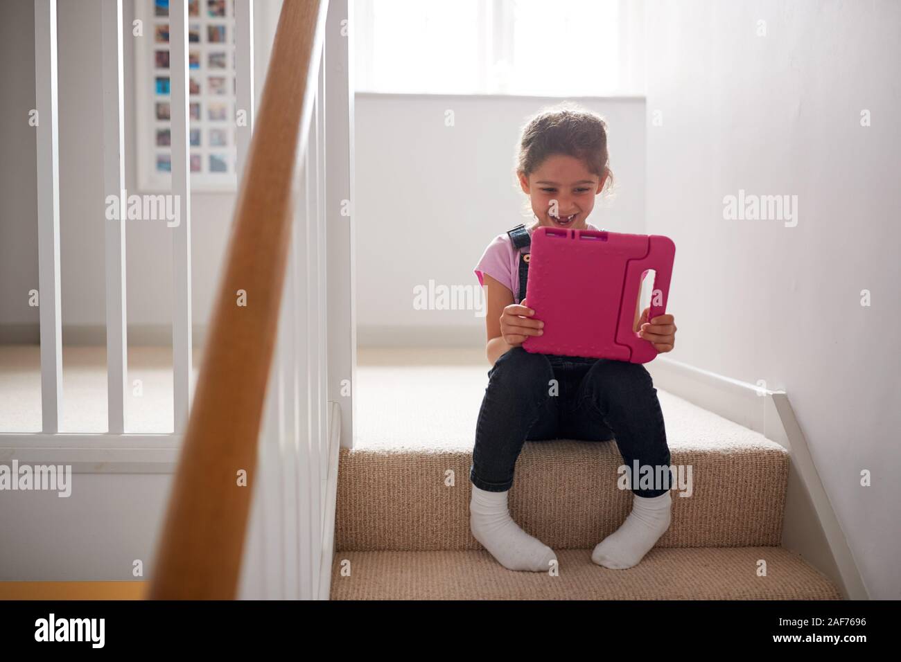 Girl Sitting On Stairs At Home Playing With Digital Tablet Stock Photo