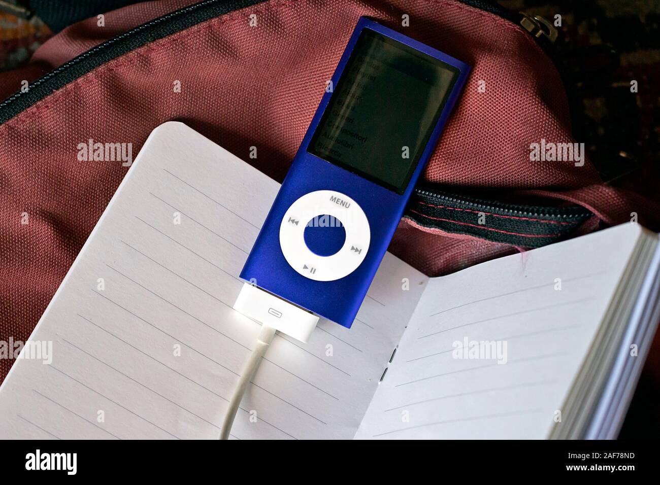 Milan, Italy - June 4, 2019.Apple iPod Nano 8Gb, blue  Music Player with charger cable attached on notebook and schoolbag background Stock Photo