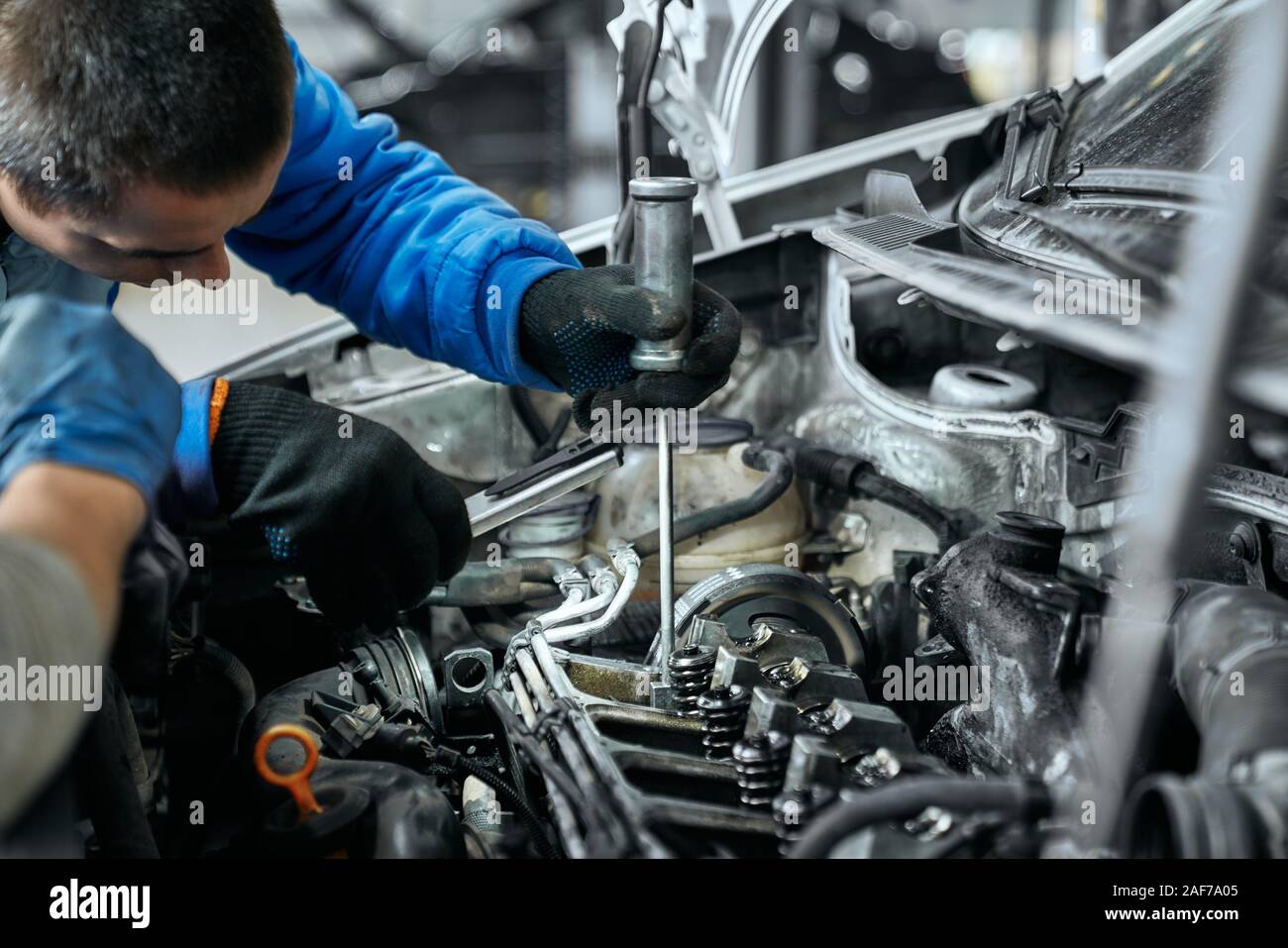Auto mechanic in blue uniform and black gloves replacing glow plugs in car  diesel engine using spark plug spanner. Qualified repairman fixing vehicle'  Stock Photo - Alamy
