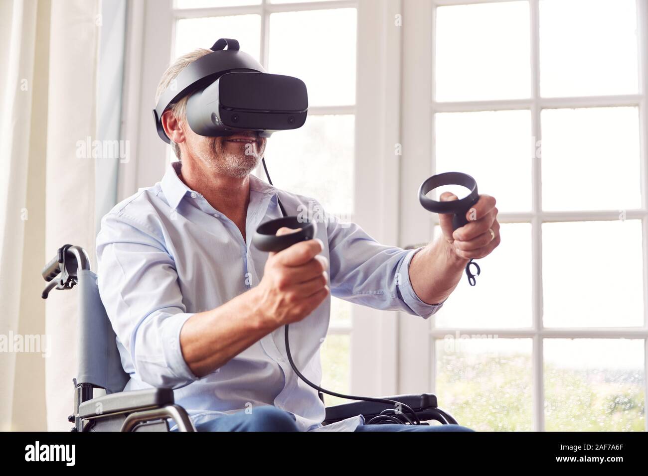 Mature Disabled Man In Wheelchair At Home Wearing Virtual Reality Headset Holding Gaming