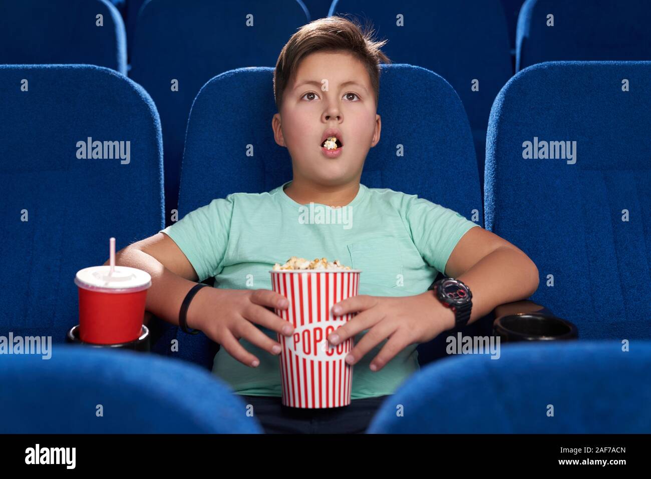 Shocked male teen with opened mouth eating popcorn and drinking sweet