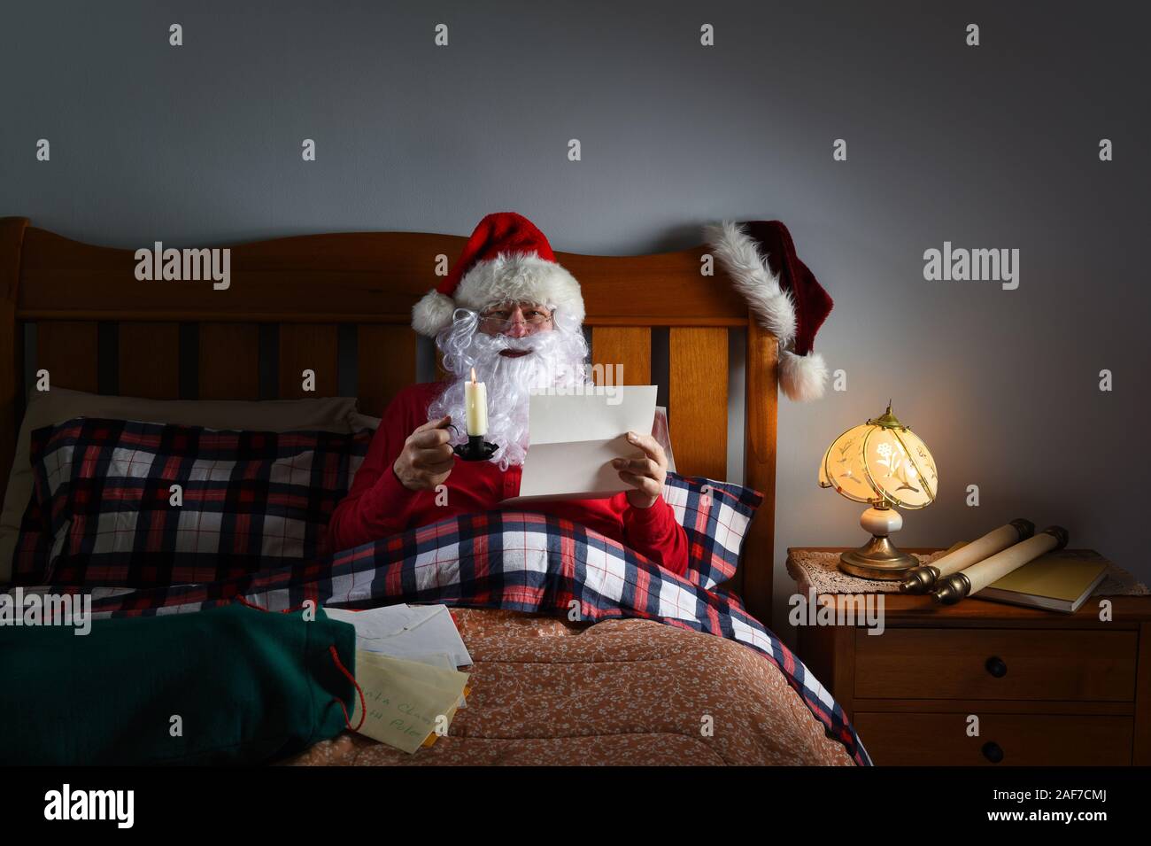 Santa Claus reading letters by candlelight in bed at his North Pole home. Stock Photo