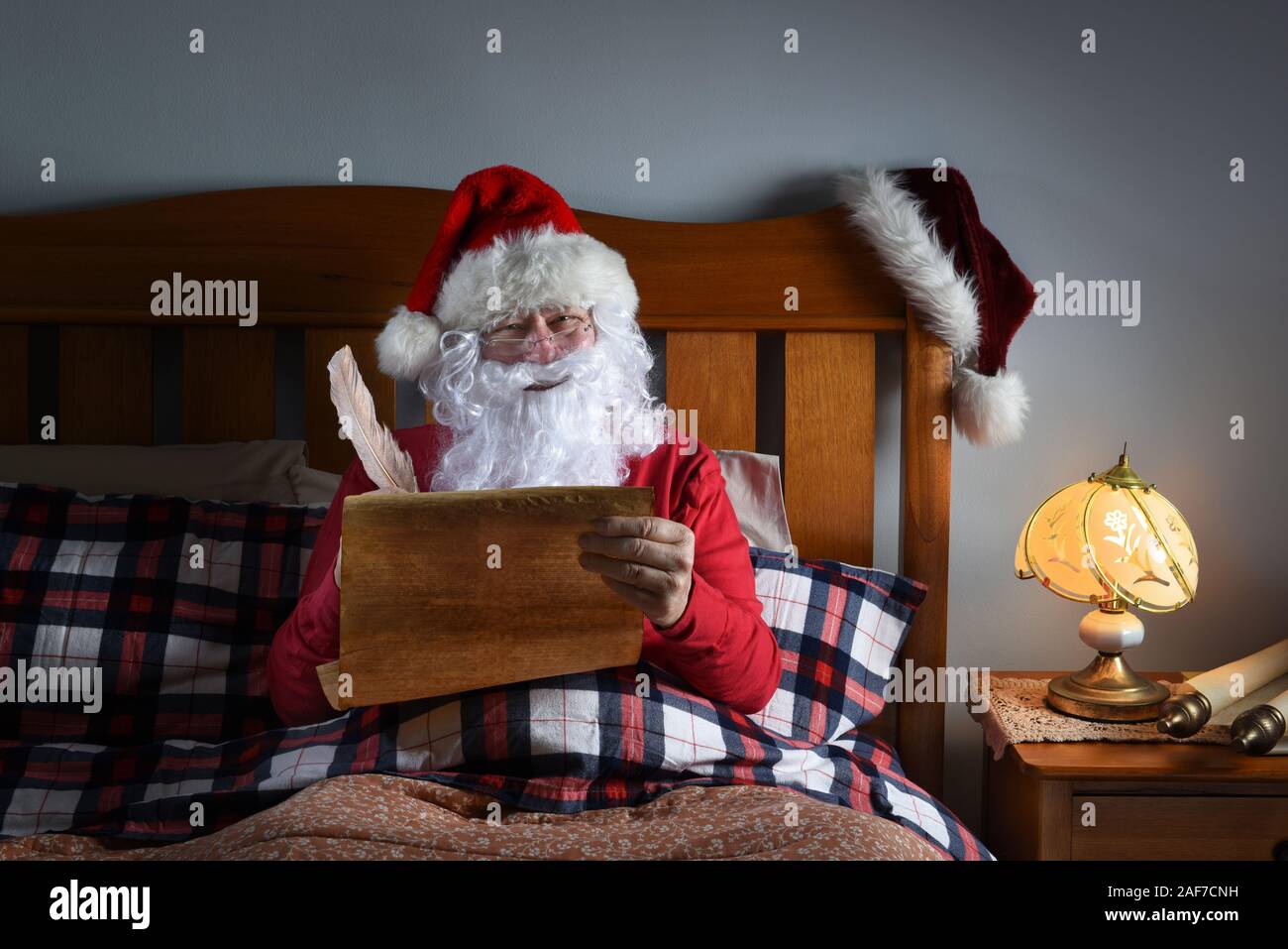 Santa Claus sitting up in his bed working on his naughty and nice list. Stock Photo