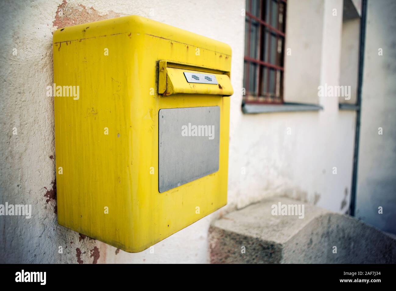 A bright yellow post box on the wall, close up. Stock Photo