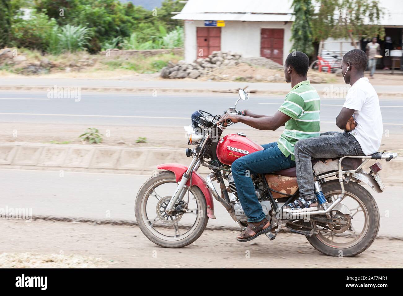 Tanzania, Mto wa Mbu Street Scene, Young Men on Motorbike, in Casual Clothing. Stock Photo