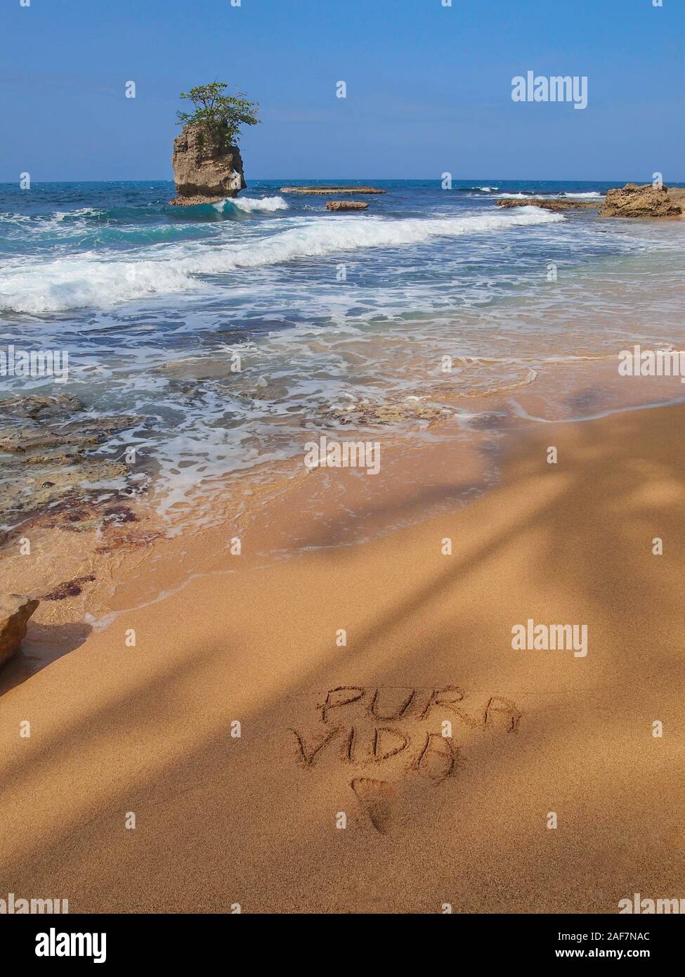 Tropical sea shore with a rocky islet and the words 'PURA VIDA' written in the sand, Caribbean coast of Costa Rica, Central America Stock Photo