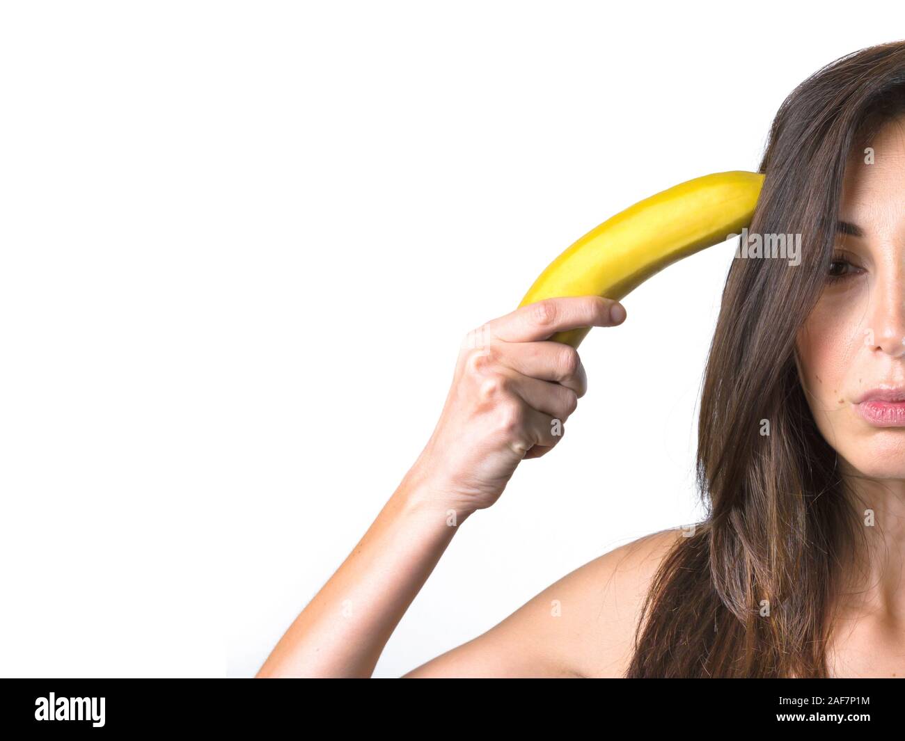 Woman holds a banana near her head in the manner of a revolver. Space for text. Stock Photo
