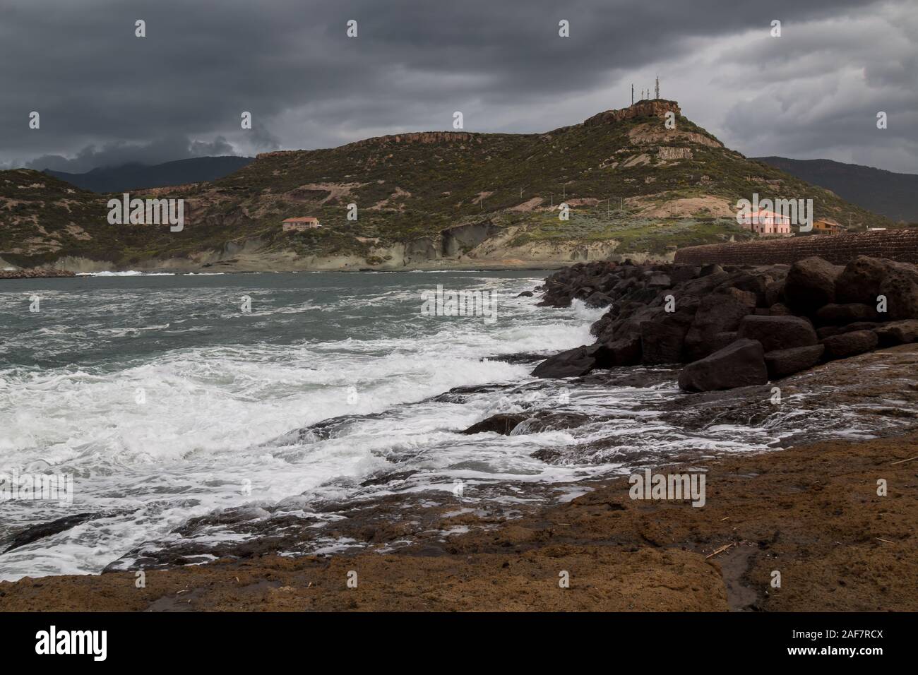 Wild waves of the Mediterranean sea in the spring, during a stormy weather. Mountain in the background. Cloudy sky. Bosa Marina, Sardinia, Italy. Stock Photo