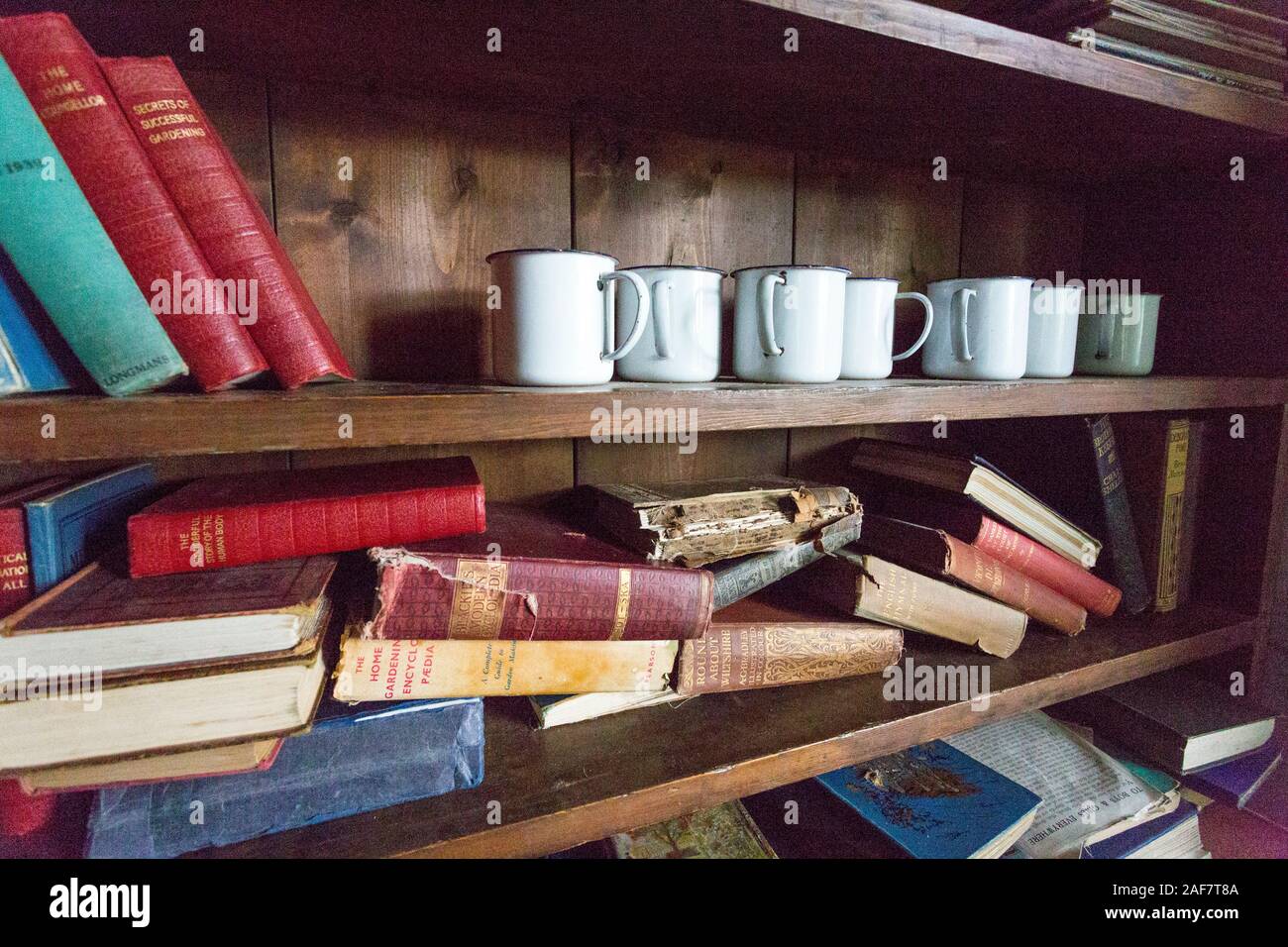 Bookshelves in the preserved schoolroom containing books unread since the 1930s in the abandoned village of Tyneham, Dorset, England, UK Stock Photo