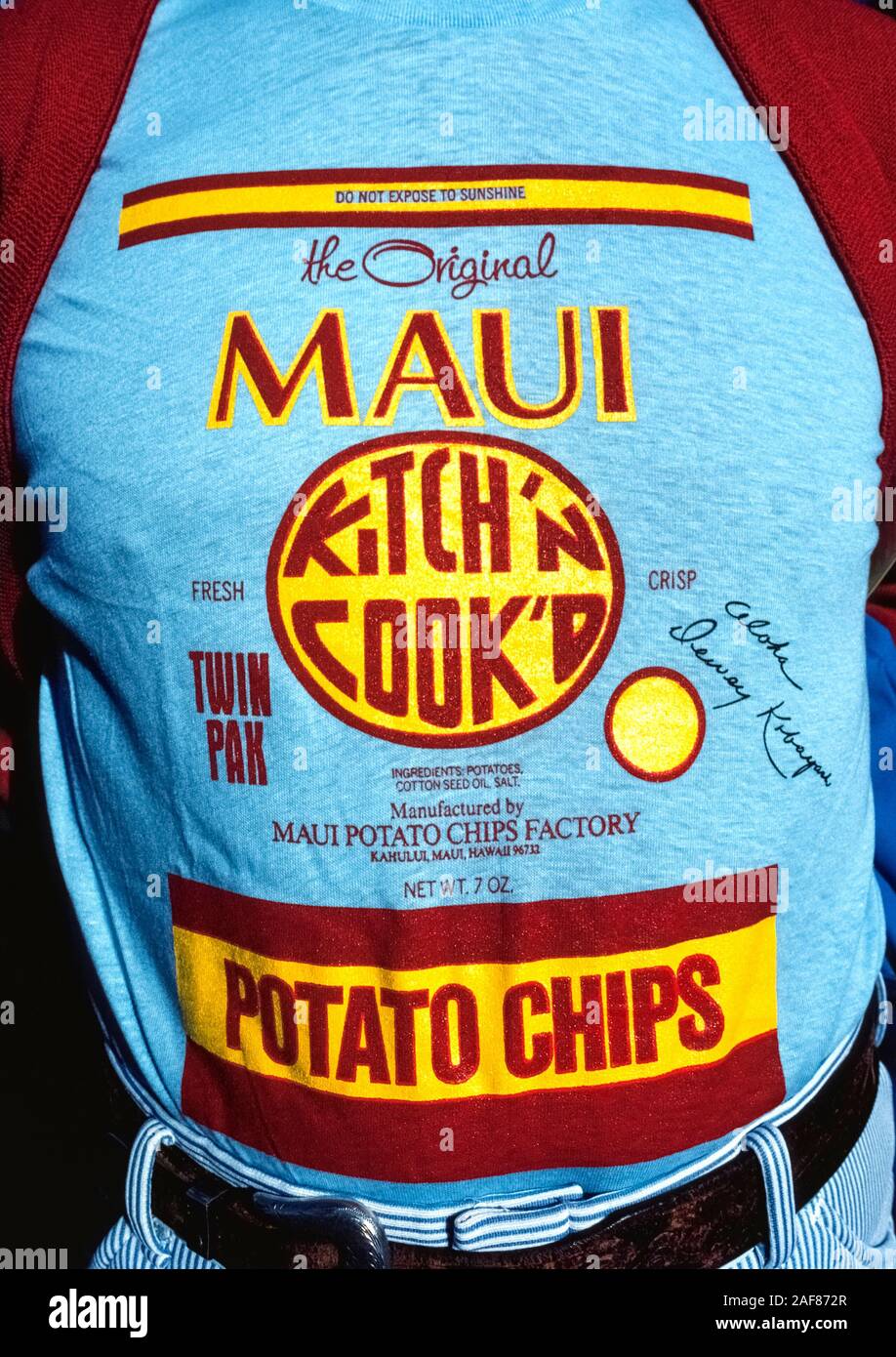 A man wears a blue shirt that replicates the front of an actual package of Maui Potato Chips, a famous snack made in Maui since 1956 that is known throughout the Hawaiian Islands, USA.  Although other makers now call their brands 'Maui' potato chips, the original product is identified by its red and yellow label and round 'Kitch'n Cook'd' logo. The 'Do Not Expose To Sunshine' warning is because the chips are packaged in clear plastic bags and the sun's UV rays and heat will cause the chips to go soft and taste stale since no chemical preservatives are used. Stock Photo