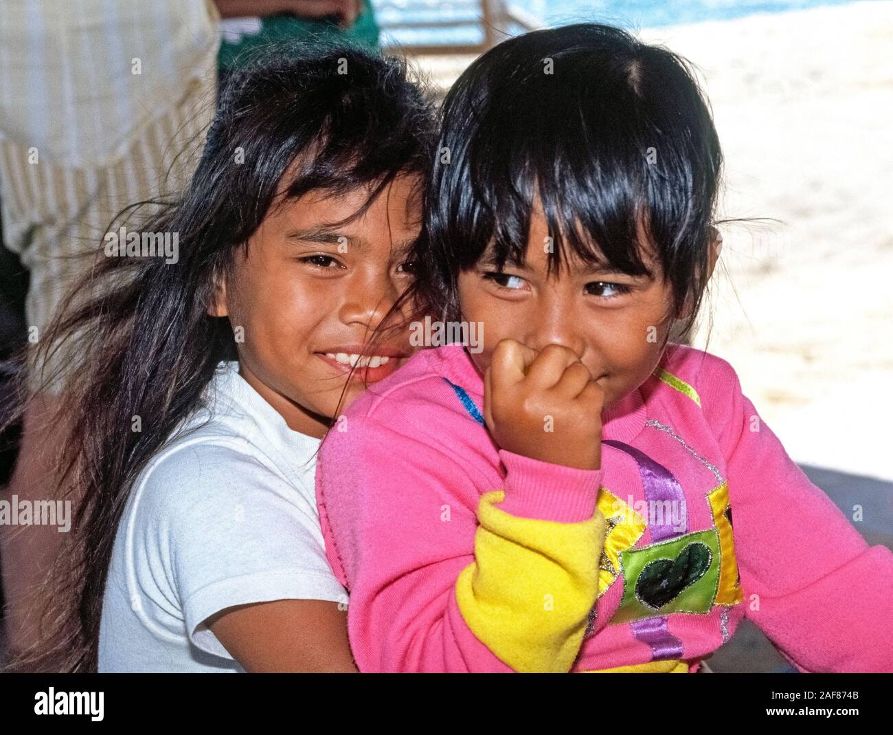 Two young Native Hawaiian girls smile at visitors to Niihau, an isolated Pacific Ocean island in Hawaii, USA. It  is known as the Forbidden Island because only Niihauans born on the island are permitted to live there and tourists are limited to a helicopter excursion to visit its shores for only a few hours. Privately owned by the same family since they purchased it from the king of Hawaii in 1864, the 72-square-mile island has less than 170 residents and is dedicated to preserving traditional Hawaiian culture. Niihau has no paved roads or running water; food is brought in by boat. Stock Photo