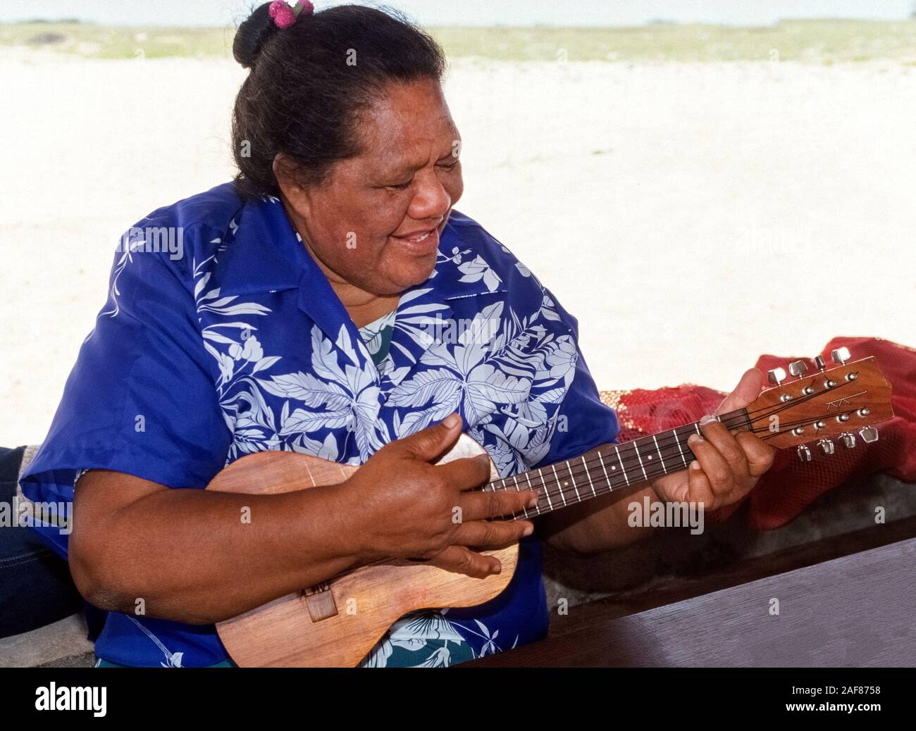 A Native Hawaiian woman entertains with song and her ukelele a few visitors to Niihau, an isolated Pacific Ocean island in Hawaii, USA. It is known as the Forbidden Island because only Niihauans born on the island are permitted to live there and tourists are limited to a helicopter excursion to visit its shores for only a few hours. Privately owned by the same family since they purchased it from the king of Hawaii in 1864, the 72-square-mile (187 square-kilometer) island has less than 170 residents and is dedicated to preserving traditional Hawaiian culture. Stock Photo