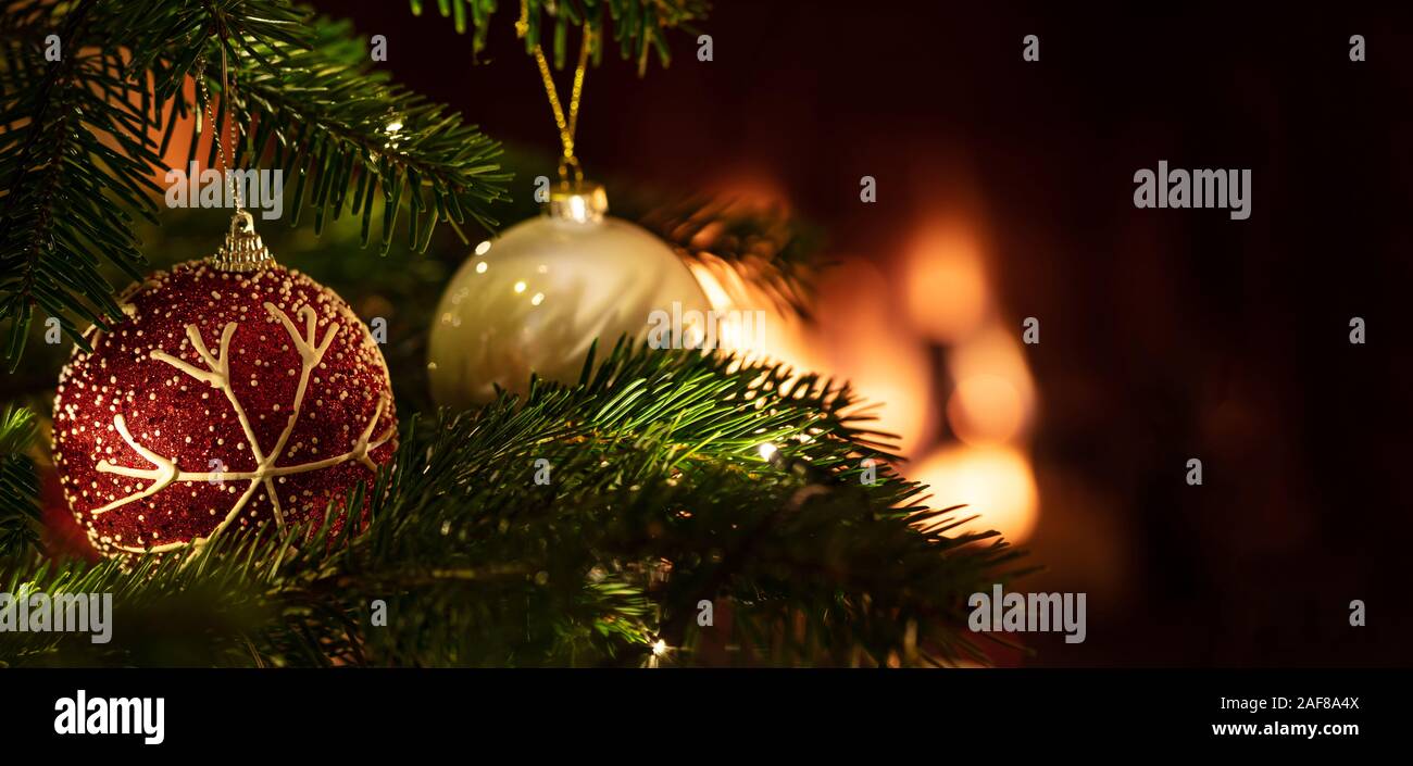 Christmas ball closeup, blur glowing fireplace background. Xmas tree ornament, copy space, banner. Warm cozy holiday home Stock Photo