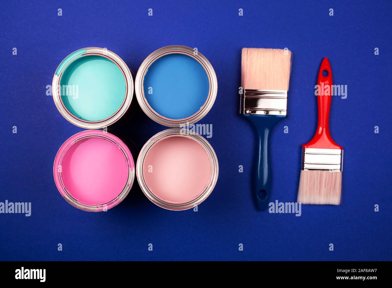 Four open cans of paint with brushes on blue background. Yellow, blue