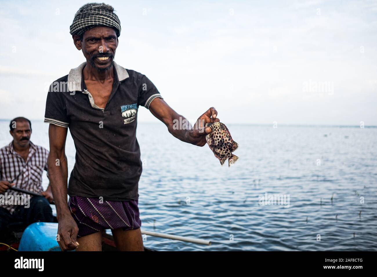 Vembanad lake, Kerala - 20 october 2019: portrait of an indian fisherman on a boat fishing and showing fish, a symbol of indian economy and food crisi Stock Photo