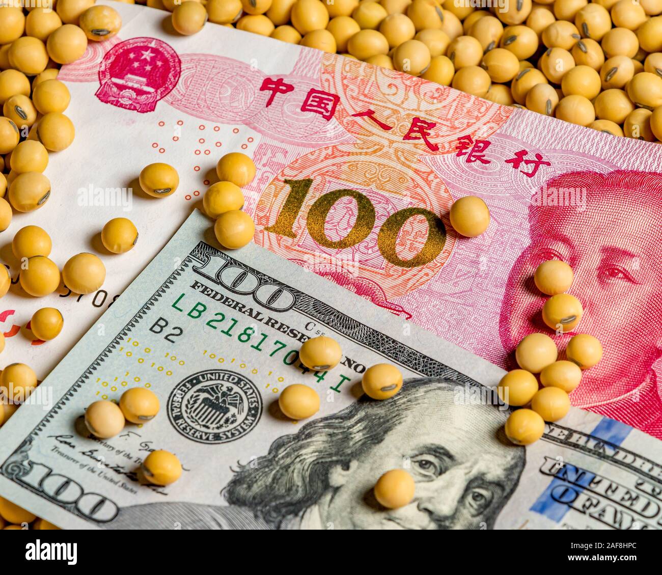 Chinese 100 yuan renminbi and American 100 dollar bill surrounded with soybeans. Concept of China & United States of America trade war, tariffs Stock Photo