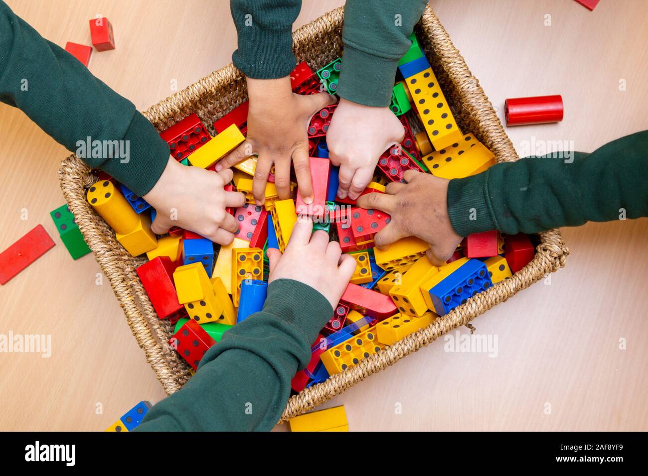 Five children's arms grabbing toy building bricks in a UK primary classroom Stock Photo
