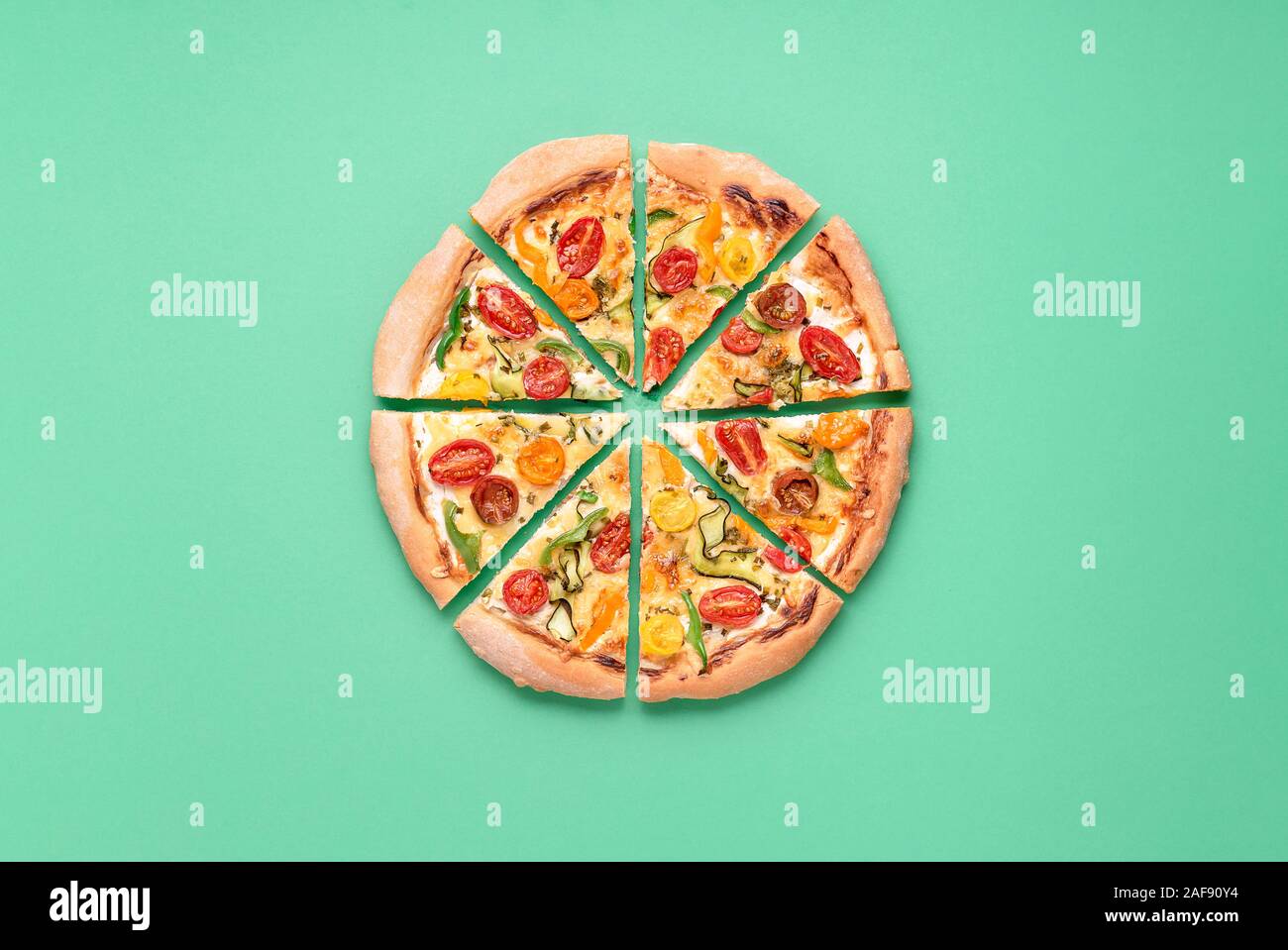 Whole pizza primavera cut in slices on a green background. Above view of vegetarian pizza