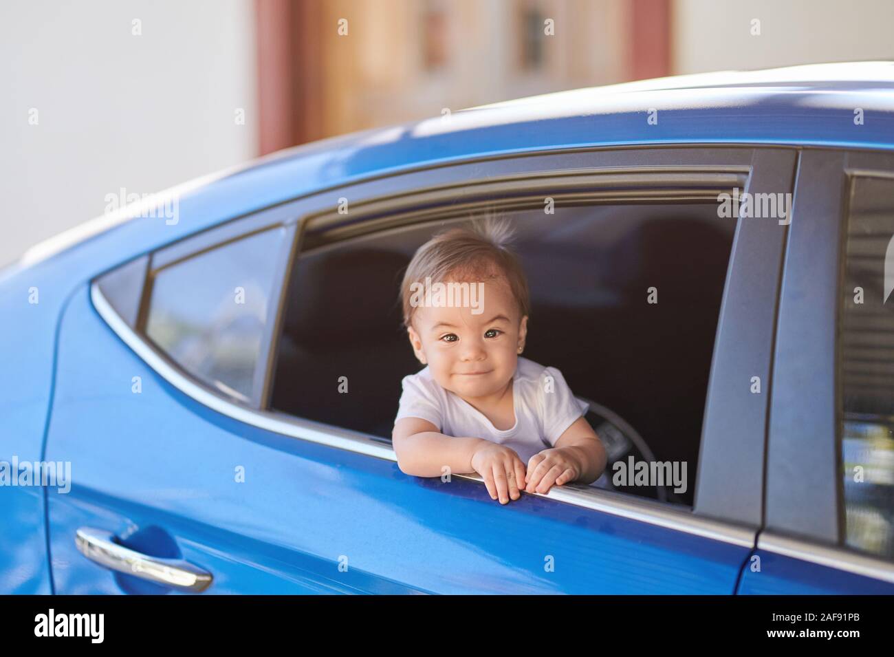 Happy baby girl looking from  car window on bright sunny day Stock Photo