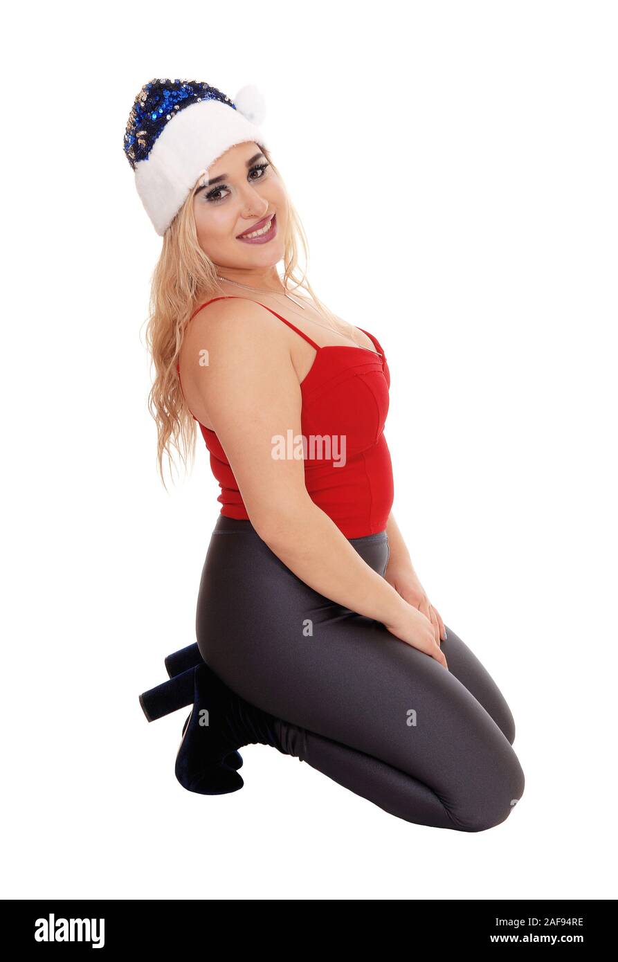 Beautiful young woman kneeling on the floor in a red top and gray  tights with a Santa hat, isolated for white background Stock Photo