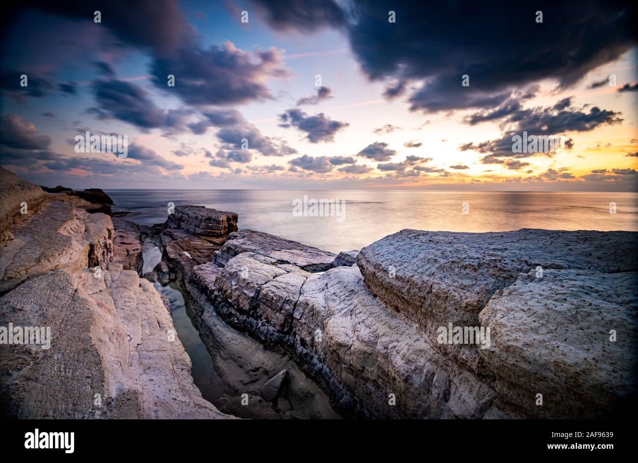 Rocky seashore seascape with wavy ocean and dramatic and beautiful sunset at sea caves coastal area  in Paphos, Cyprus Stock Photo