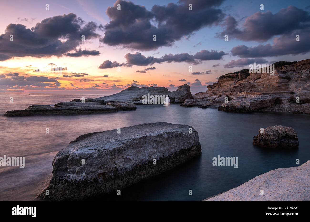 Rocky seashore seascape with wavy ocean and dramatic and beautiful sunset at sea caves coastal area  in Paphos, Cyprus Stock Photo