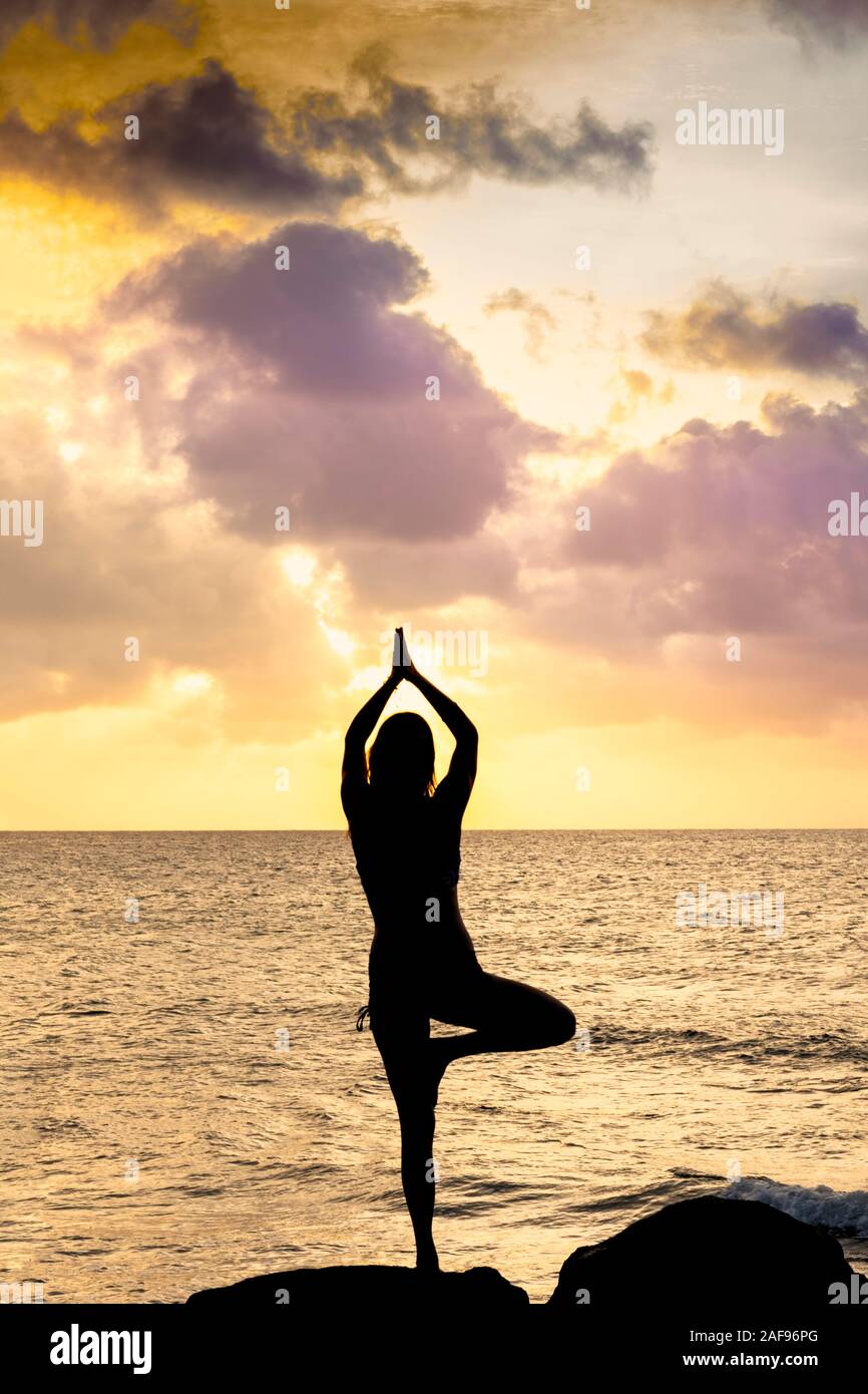 A young woman in a yoga asana shot against the ocean and a golden Sunscape Stock Photo