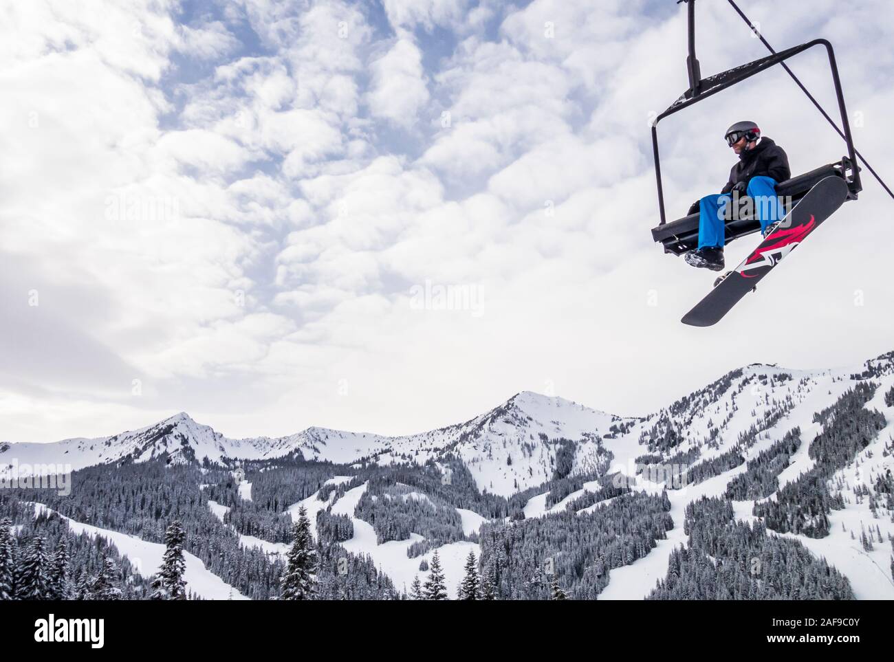 A snowboarder sitting on a chairlift above Crystal Mountain Resort, Washington State, USA. Stock Photo