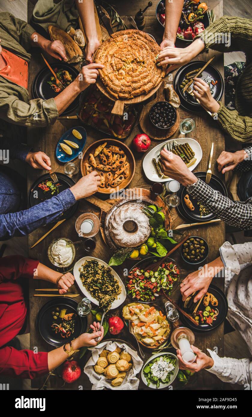 Traditional Turkish family celebration dinner. Flat-lay of people feasting at table with Turkish salads, cooked vegetables, meze starters, borek pie a Stock Photo