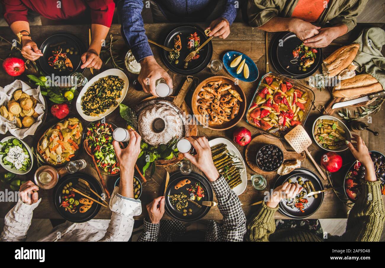 Traditional Turkish celebration dinner. Flat-lay of people eating Turkish salads, cooked vegetables, meze starters, pastries and drinking raki drink, Stock Photo